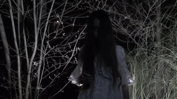Ένα μικρό κορίτσι της φάντασμα με μακριά μαύρα μαλλιά, λευκό, περιφέρεται μέσα στο δάσος με ένα μαχαίρι και ένα μαλακό παιχνίδι. 4k — Αρχείο Βίντεο