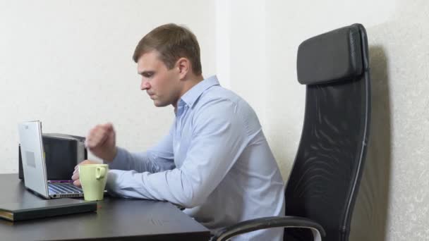 Молодой человек налил чай в ноутбук. работает в офисе. Съемка замедленного действия, 4k — стоковое видео