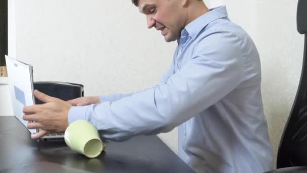 A young man poured tea onto a laptop. works in the office. Slow-motion shooting, 4k — Stock Video