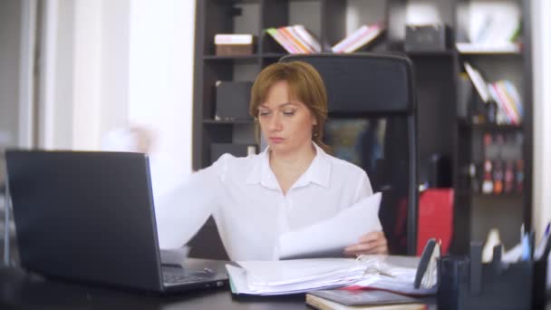 Una mujer de negocios que escanea documentos, frunce el ceño, utilizando un ordenador portátil, no realiza una tarea urgente en la oficina, no hay tiempo suficiente, 4k. la oficina está caliente, el aire acondicionado no funciona — Vídeo de stock