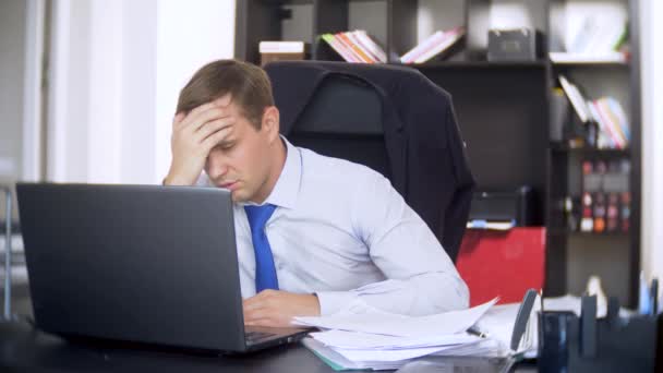 Un homme d'affaires qui scanne des documents, fronce les sourcils, à l'aide d'un ordinateur portable, n'effectue pas une tâche urgente dans le bureau, il n'y a pas assez de temps, 4k. le bureau est chaud, la climatisation ne fonctionne pas — Video