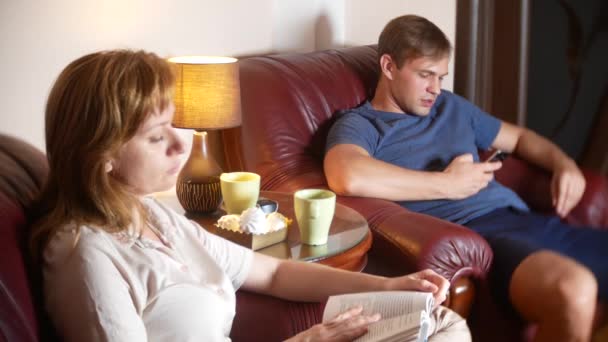 Interne en communicatie probleem in de familie. de man maakt gebruik van zijn smartphone, de vrouw leest het boek negeren elkaar. 4k. — Stockvideo