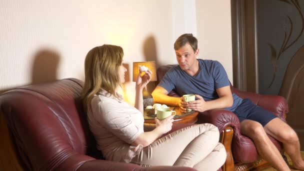 Pareja feliz marido y mujer están sentados en casa en la sala de estar, hablando relajarse y beber té tarde en la noche. 4k — Vídeos de Stock