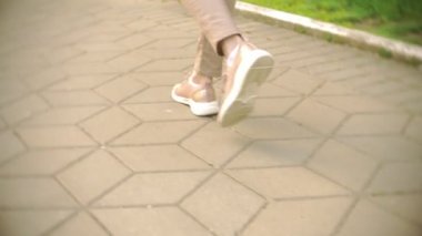 ince kadın bacakları bej pantolon ve spor ayakkabı açık güneşli bir günde parkta yürüyüş yapın. 4k, ağır çekim