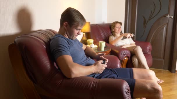 Una pareja casada sentada en una silla y viendo televisión en casa juntos. 4k, tarde en la noche, oscuro . — Vídeos de Stock