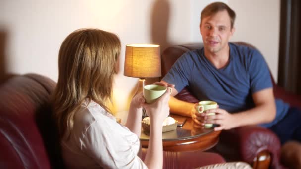 幸せカップル夫と妻は家で座っているリビング ルームで話してリラックスし、夜遅くまでお茶を飲みます。4 k — ストック動画