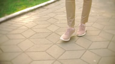 ince kadın bacakları bej pantolon ve spor ayakkabı açık güneşli bir günde parkta yürüyüş yapın. 4k, ağır çekim
