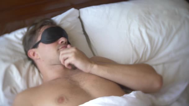 Ung man i en mask för att sova, sover i sängen på en kudde på dagtid. 4k. — Stockvideo
