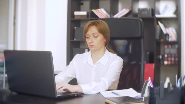 Woman working in office with documents and laptop. she looks at the camera and smiles 4k. — Stock Video