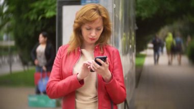 otobüs durağında duran ve bir cep telefonu kullanarak kadın. 4k