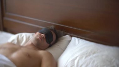 Bir yastık üzerine yatakta gündüz uyku uyumak için bir maske içinde genç adam. 4k.