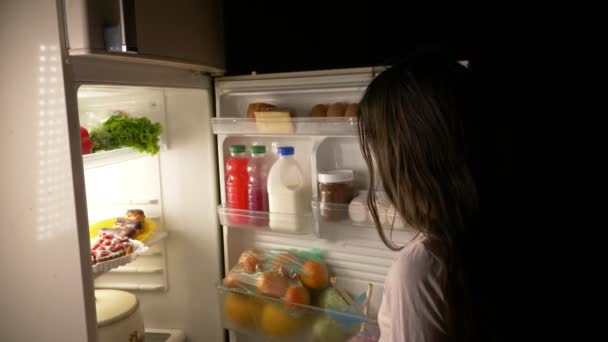 Chica adolescente abre el refrigerador por la noche. hambre nocturna. dieta. gula, 4k — Vídeo de stock