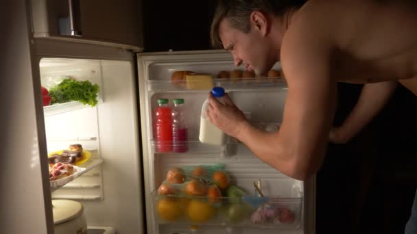 Ein junger muskulöser Mann öffnet nachts den Kühlschrank. Nachthunger. Ernährung. Völlerei, 4k — Stockvideo