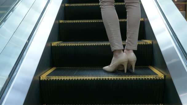 4k των ποδιών μιας γυναίκας σε μπεζ παντελόνι, σε μπεζ παπούτσια που στέκεται πάνω σε ένα κινούμενο κυλιόμενες σκάλες — Αρχείο Βίντεο