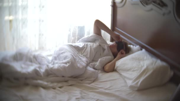 Jonge vrouw in een masker voor het slapen, slapen in bed op een kussen overdag. 4k. — Stockvideo