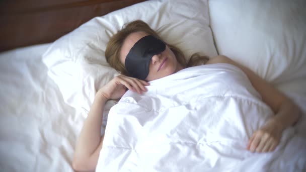 Jonge vrouw in een masker voor het slapen, slapen in bed op een kussen overdag. 4k. — Stockvideo