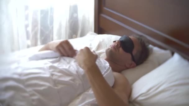 Jeune homme masqué pour dormir, dormant au lit sur un oreiller le jour. 4k . — Video