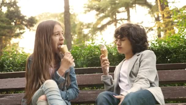 Милые подростки, мальчик и девочка едят мороженое в парке и разговаривают. 4k — стоковое видео