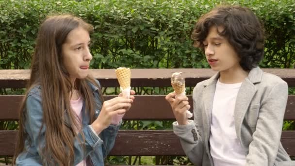 Cute teenagers, boy and girl eating ice cream in the park and talking. 4k — Stock Video