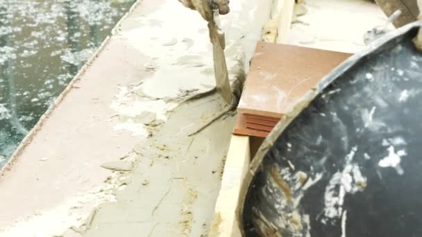 Лопатка и ведро с раствором на строительной площадке. строитель заканчивает поверхность штукатуркой. 4k. ремонт бассейна . — стоковое видео