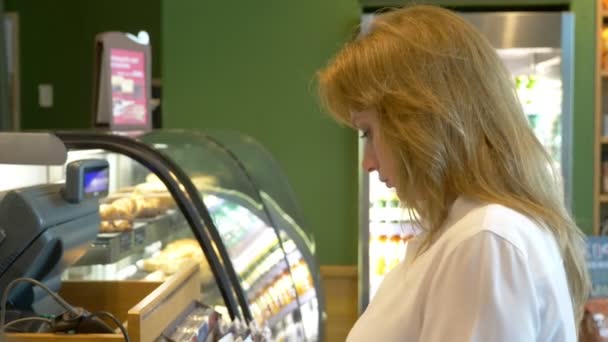 Een vrouw op zoek naar een glazen vitrine in de winkel. 4k, achtergrond vervagen. — Stockvideo