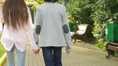 Arkadan Görünüm. genç oğlan ve kız elele sokak park boyunca yürüyüş. 4k