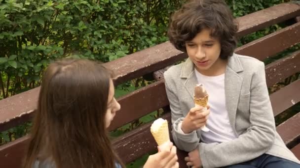 かわいい 10 代の若者、男の子と女の子公園でアイスクリームを食べると話しています。4 k — ストック動画