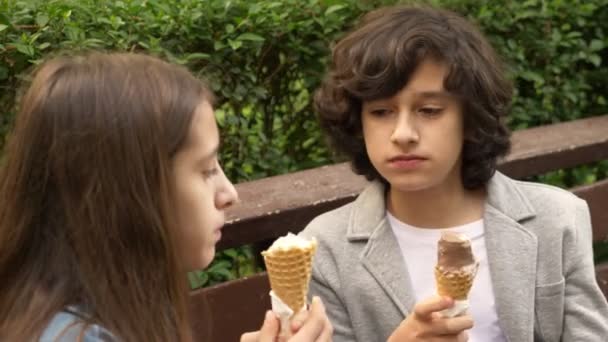 Милые подростки, мальчик и девочка едят мороженое в парке и разговаривают. 4k — стоковое видео