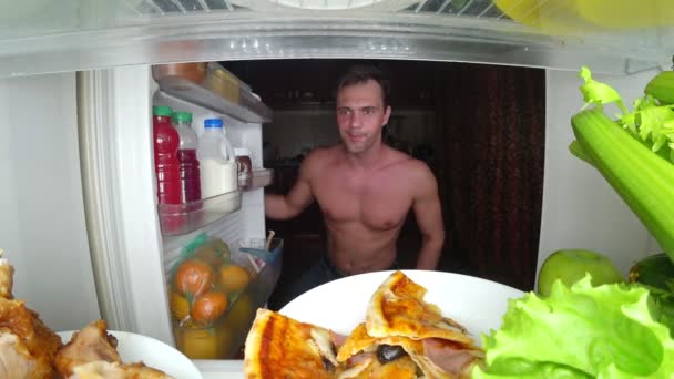 Молодой мускулистый человек открывает холодильник ночью. ночной голод. диета. glenony, 4k — стоковое видео