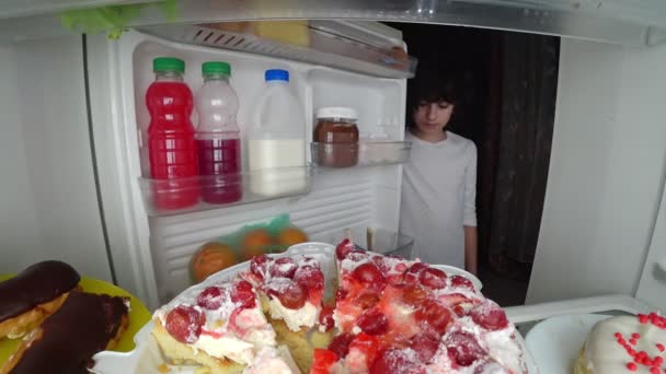 Niño comiendo frente al refrigerador en medio de la noche. 4k — Vídeo de stock