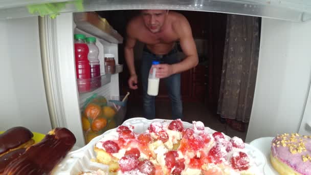 Svalnatý mladík otevírá lednici v noci. Noční hlad. strava. obžerství, 4k — Stock video