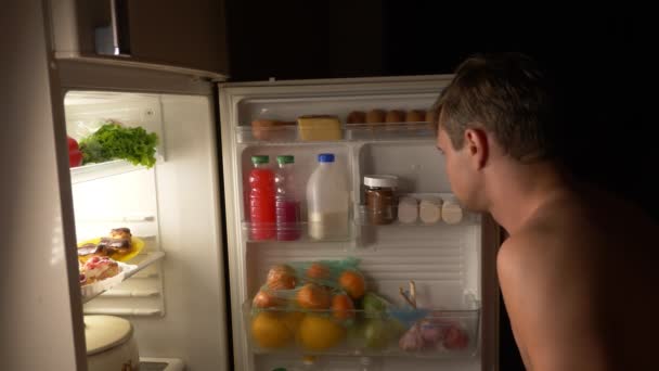 Un joven musculoso abre el refrigerador por la noche. hambre nocturna. dieta. gula, 4k — Vídeo de stock