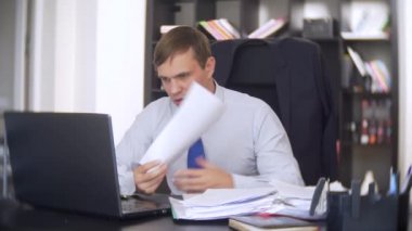 belgeler, inceden inceye gözden geçirmek bir işadamı, bir dizüstü bilgisayar kullanarak frowns, ofiste acil bir görev yapmaz, yeterli zaman değil 4k