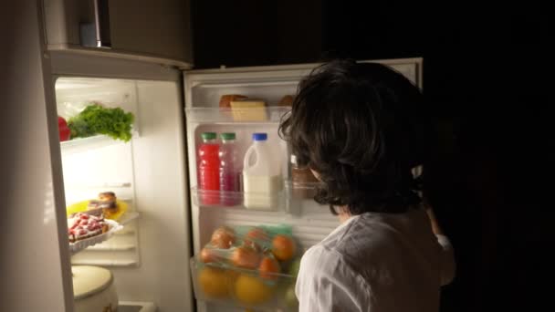 Niño comiendo frente al refrigerador en medio de la noche. 4k — Vídeo de stock