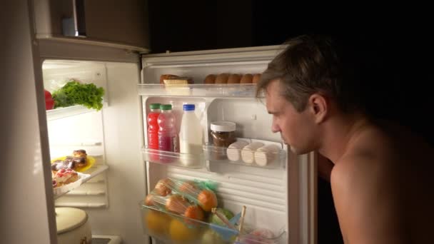Genç bir kaslı adam geceleri buzdolabı açılır. gece açlık. diyet. oburluk, 4k — Stok video