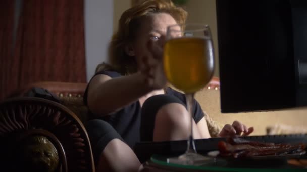 Женщина с компьютером, пьет пиво дома в темноте. 4k — стоковое видео