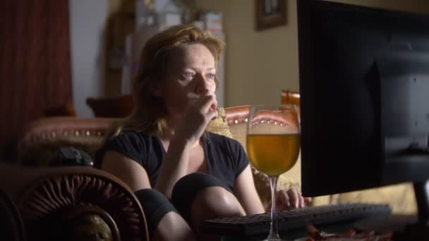 Женщина с компьютером, пьет пиво дома в темноте. 4k — стоковое видео