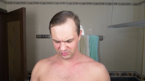 Un bell'uomo spalma una faccia con una crema davanti a uno specchio in bagno. 4k — Video Stock