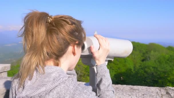 Vrouw blond reiziger kijken door een telescoop op de top van een berg. 4k, slow-motion — Stockvideo