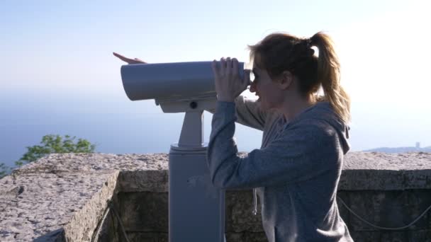 Mujer rubia viajera mirando a través de un telescopio en la cima de una montaña. 4k, cámara lenta — Vídeo de stock