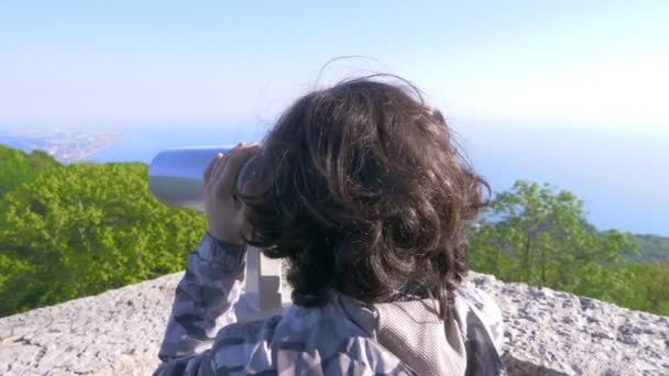 Rapaz adolescente, viajante, a olhar através de um telescópio no topo de uma montanha. 4k, câmera lenta — Vídeo de Stock