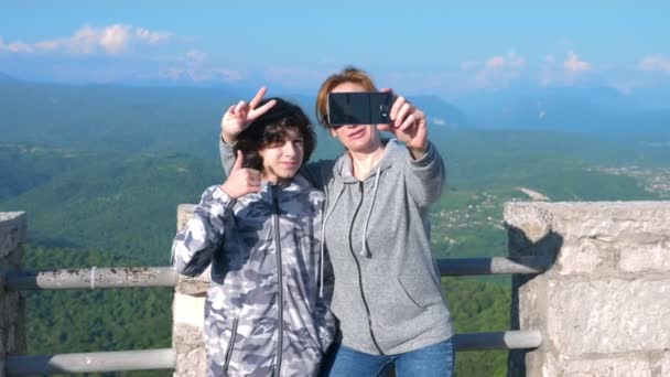 Una mujer y su hijo un adolescente haciendo sefi con una vista de las montañas magníficas. 4 k. Disparo lento — Vídeos de Stock
