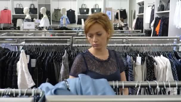 Женщина ходит по магазинам одежды, выбирает одежду. 4k — стоковое видео