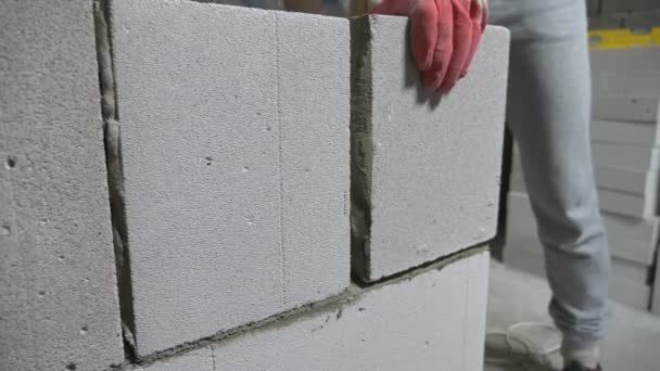 Auf einer Baustelle stellt ein Bauarbeiter eine Wand aus Gasblöcken auf. 4k. — Stockvideo