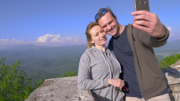 Una pareja, un hombre y una mujer hacen un sefi con vistas a las montañas magníficas. 4 k. Disparos en cámara lenta — Vídeos de Stock