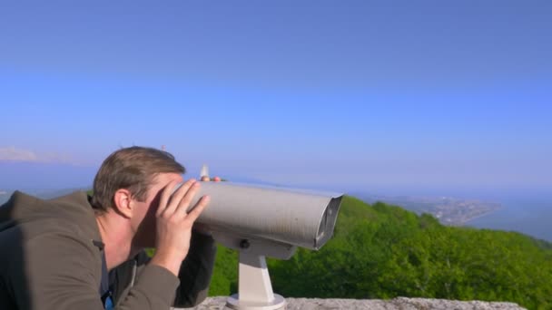 Мужчина-путешественник смотрит в телескоп на вершине горы. 4k, slow motion — стоковое видео