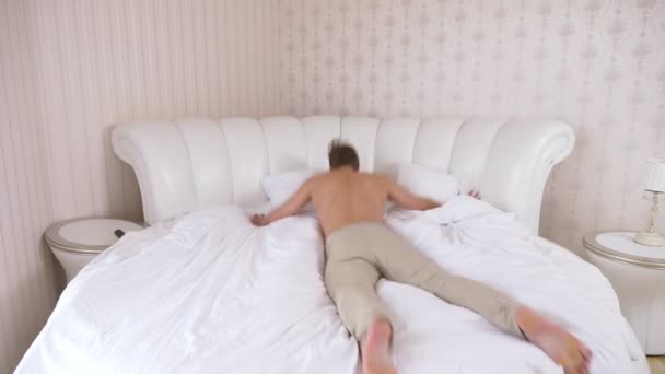 Handsome young caucasian man jumping on the bed in the bedroom. 4k, slow motion. — Stock Video