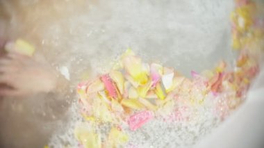 Güzel ve genç birbayan hidromasaj ve mavi bir arka plan üzerinde gül yaprakları ile bir banyoda rahatlatır. Konsept: spa yordamlar, vücut masajı, spa krem, gevşeme, su tedavileri. 4k, ağır çekim. Görünüm