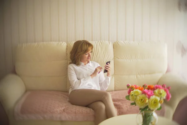 A fashionable lady dressed in a white blouse and beige trousers. A young woman uses a mobile phone indoors with an exquisite interior. — Stock Photo, Image