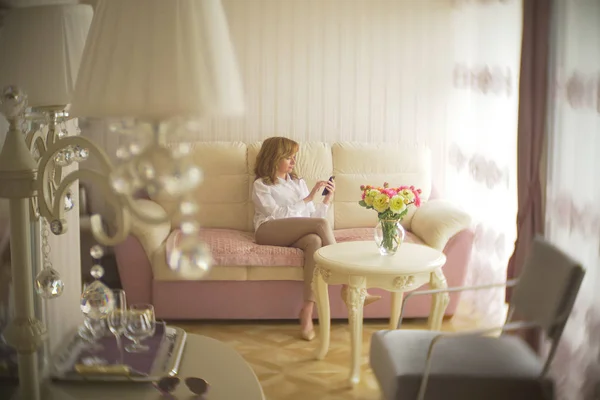 Een trendy dame gekleed in een witte blouse en een beige broek. Een jonge vrouw maakt gebruik van een mobiele telefoon binnenshuis met een prachtige interieur. — Stockfoto